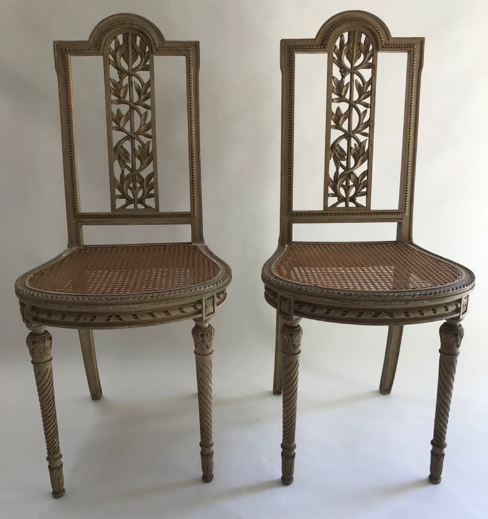 A pair of French painted timber side chairs featuring foliate back carving, woven cane seats, and spiral-turned front legs.