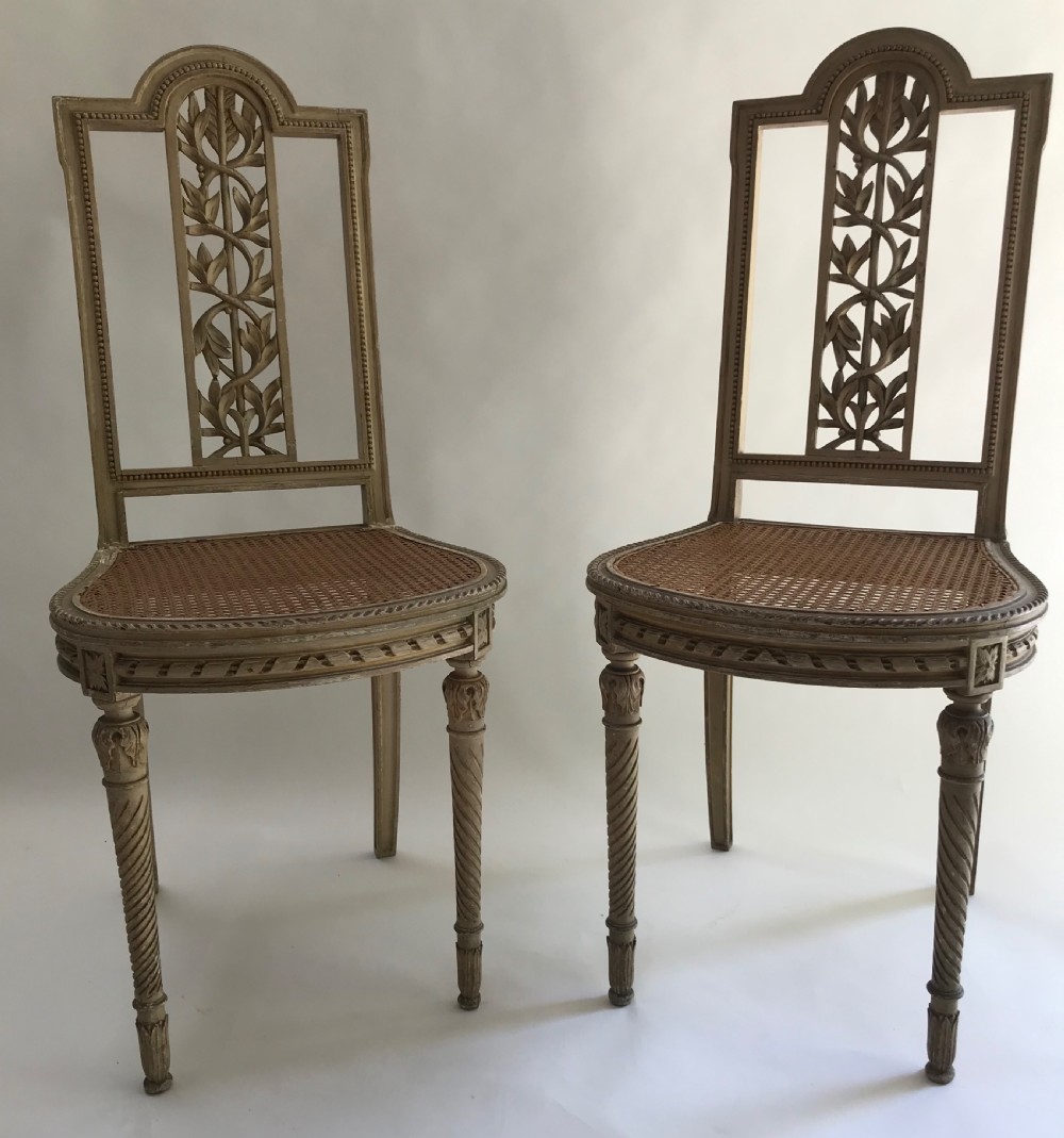 A pair of French painted timber side chairs featuring foliate back carving, woven cane seats, and spiral-turned front legs. View II