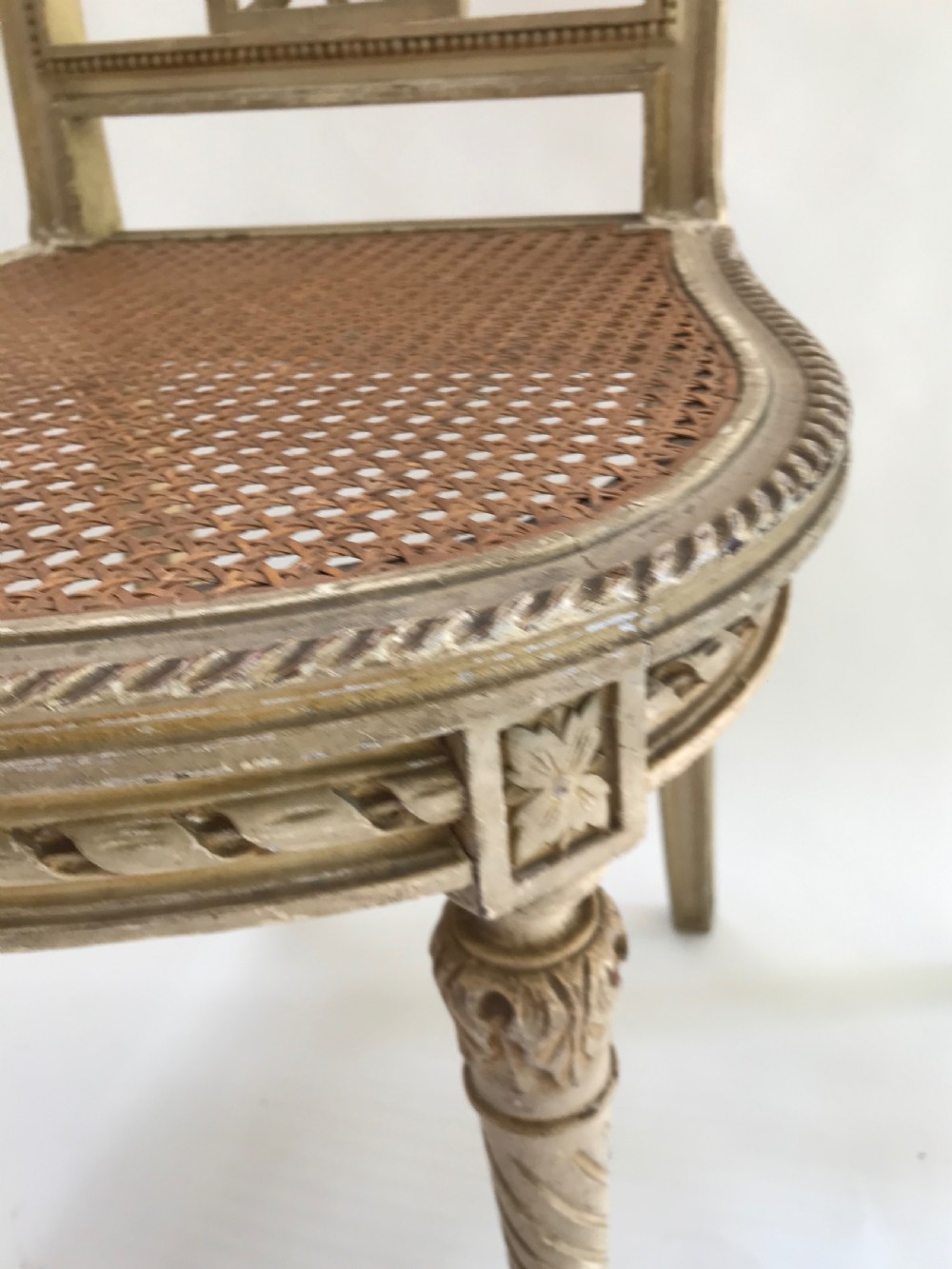 A pair of French painted timber side chairs featuring foliate back carving, woven cane seats, and spiral-turned front legs. View V