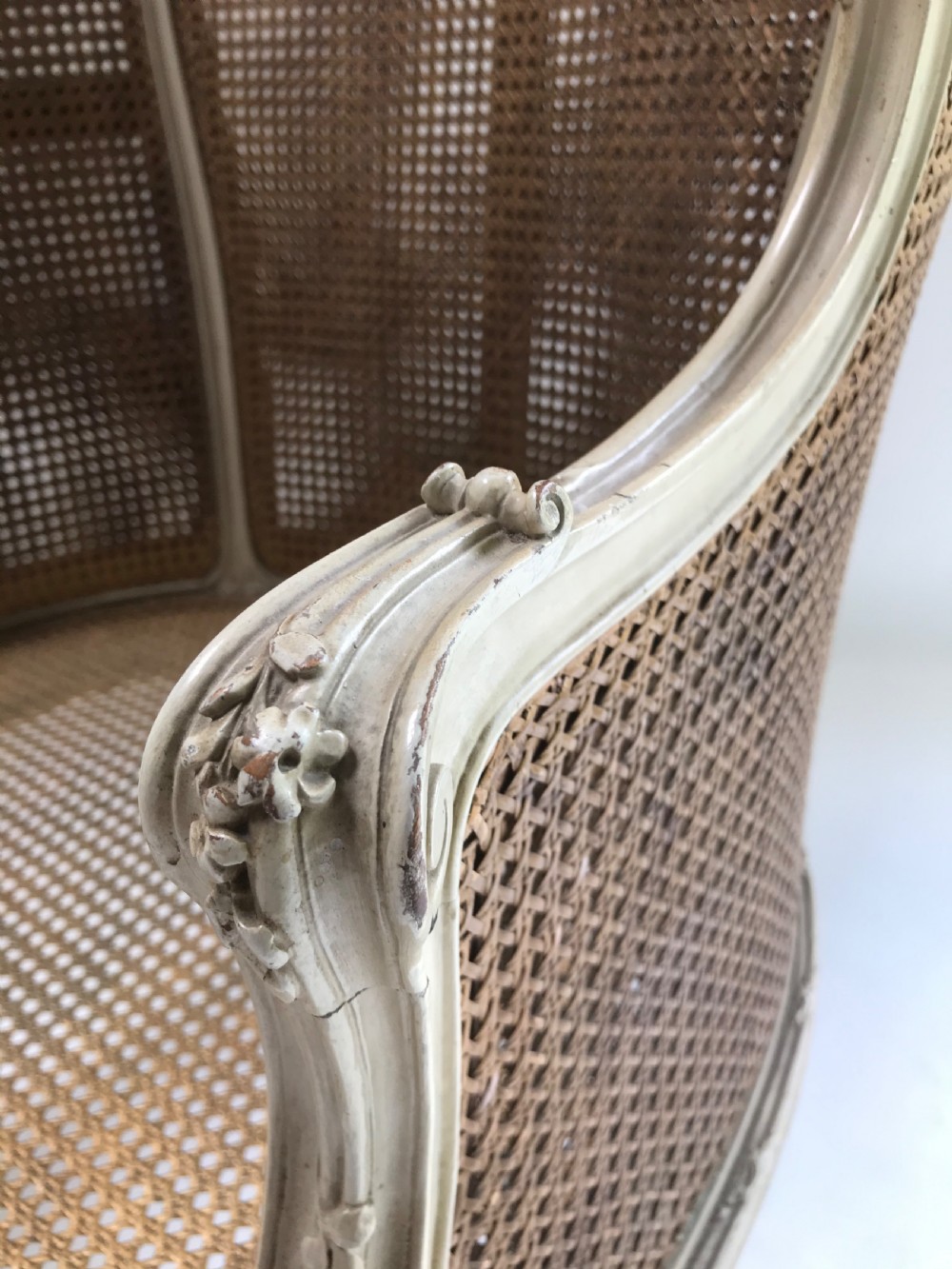 A French Louis XV style painted armchair featuring hand-woven cane back and sides, carved floral motifs, cream distressed paint finish, and cabriole legs. View II