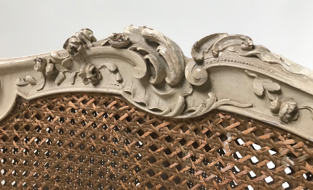 A French Louis XV style painted armchair featuring hand-woven cane back and sides, carved floral motifs, cream distressed paint finish, and cabriole legs. View IV