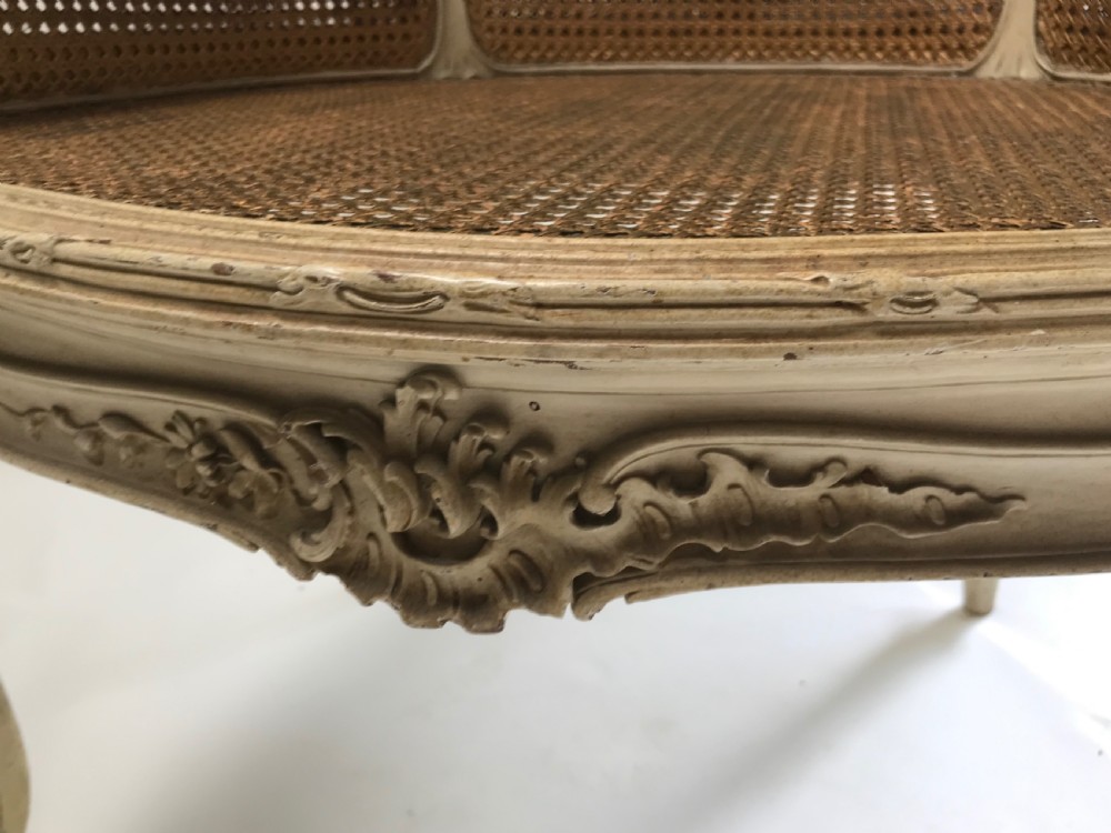 A French Louis XV style painted armchair featuring hand-woven cane back and sides, carved floral motifs, cream distressed paint finish, and cabriole legs. View V