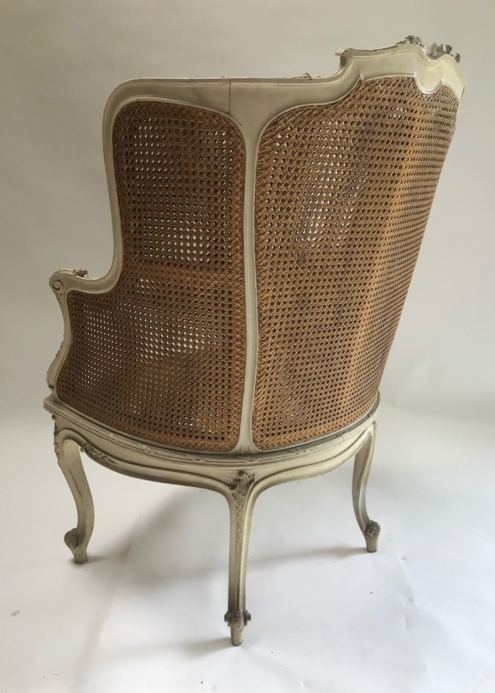 A French Louis XV style painted armchair featuring hand-woven cane back and sides, carved floral motifs, cream distressed paint finish, and cabriole legs. View VI