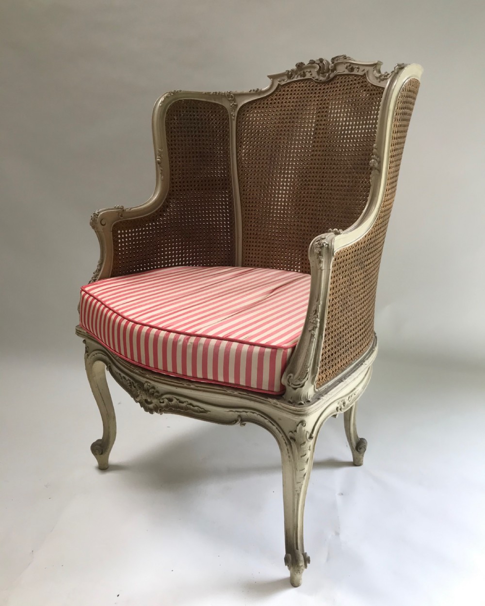 A French Louis XV style painted armchair featuring hand-woven cane back and sides, carved floral motifs, cream distressed paint finish, and cabriole legs. View VII