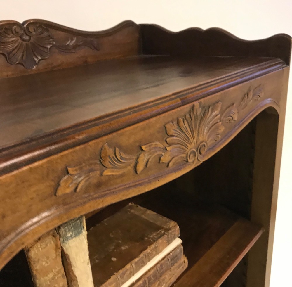 A hand-carved French walnut open bookcase featuring three shelves, carved floral cresting, panelled sides, and cabriole legs. View VI