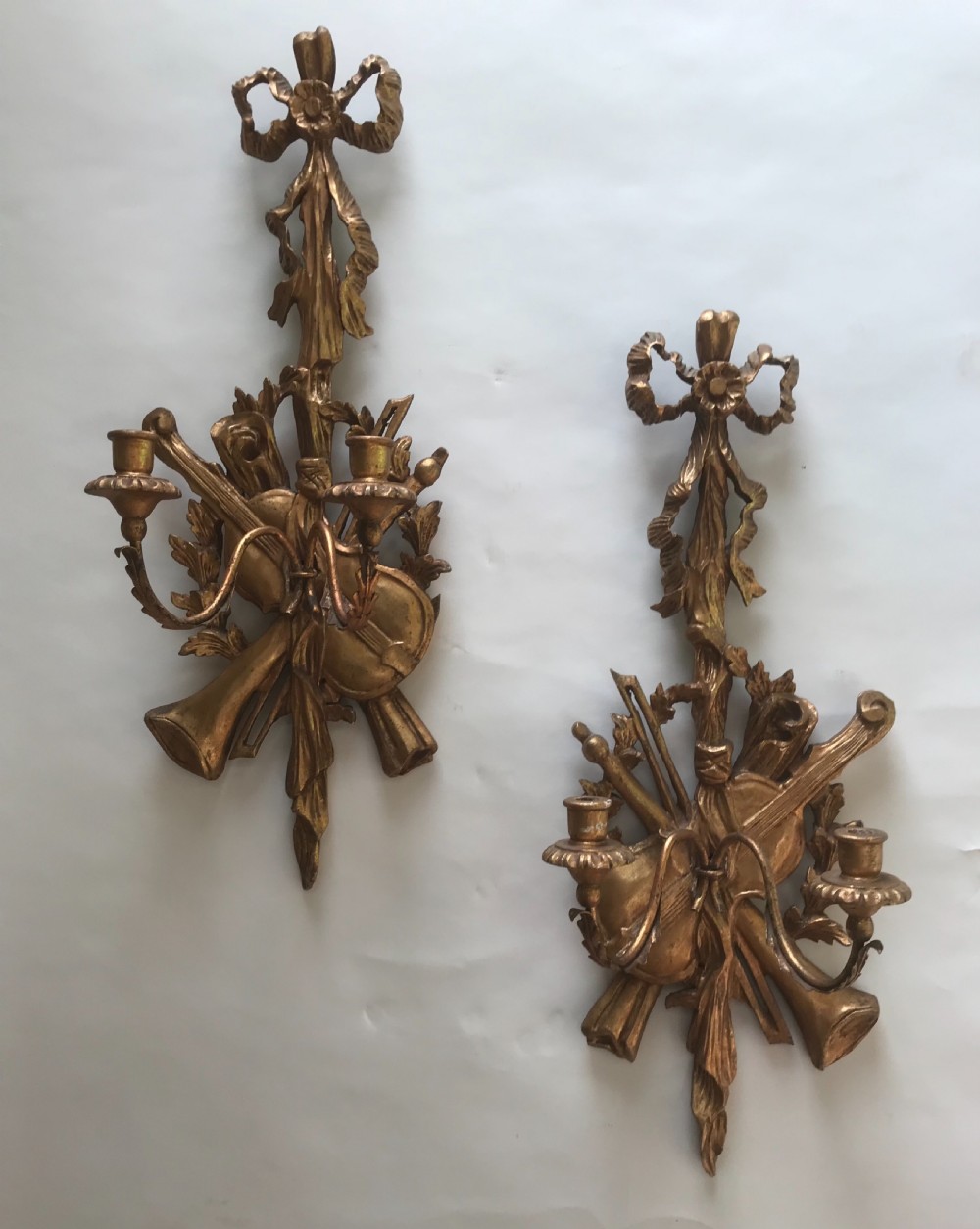 A pair of gold giltwood wall sconces carved with ribbon crests, violins, horns, and two candle branches each.