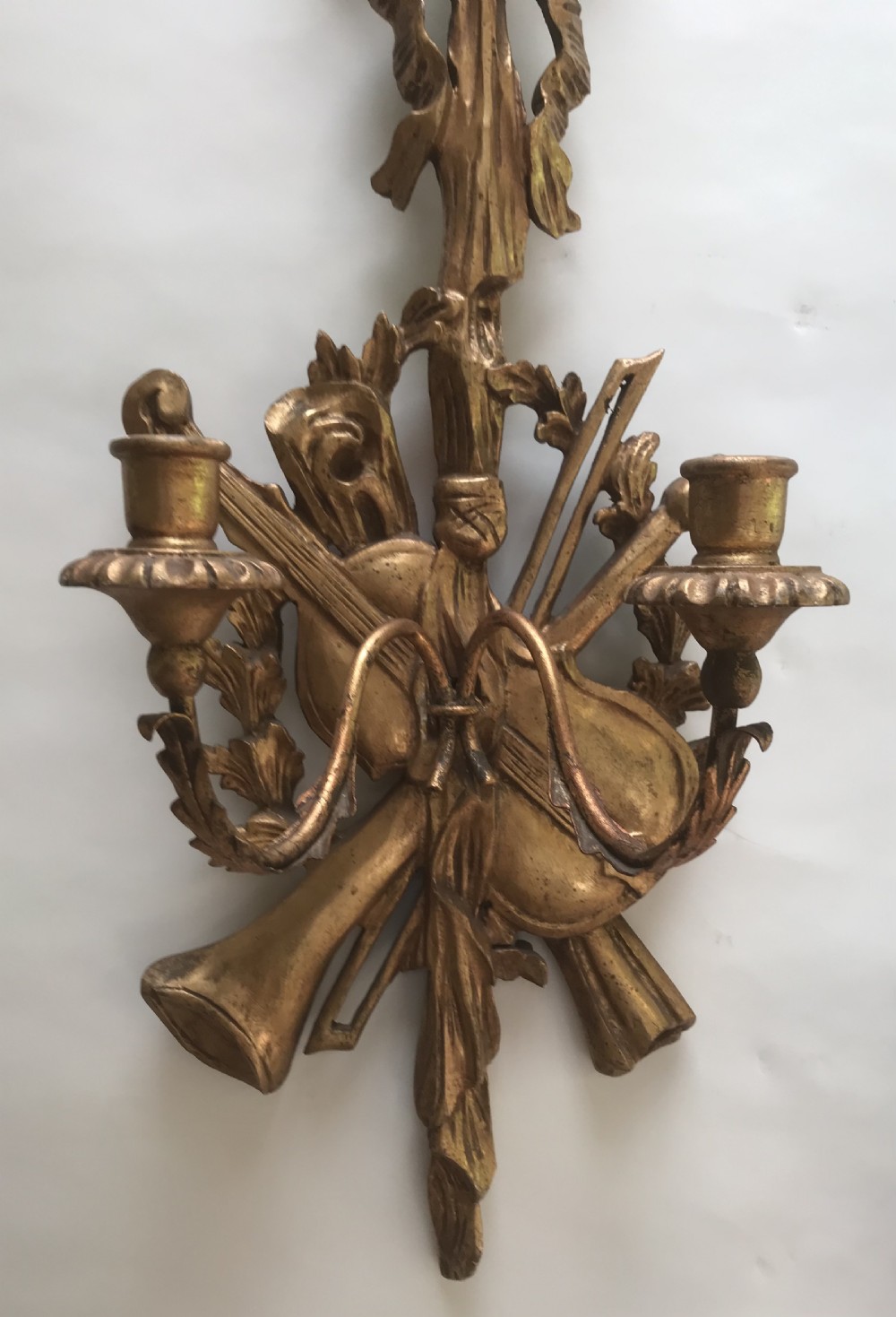 A pair of gold giltwood wall sconces carved with ribbon crests, violins, horns, and two candle branches each. View IV