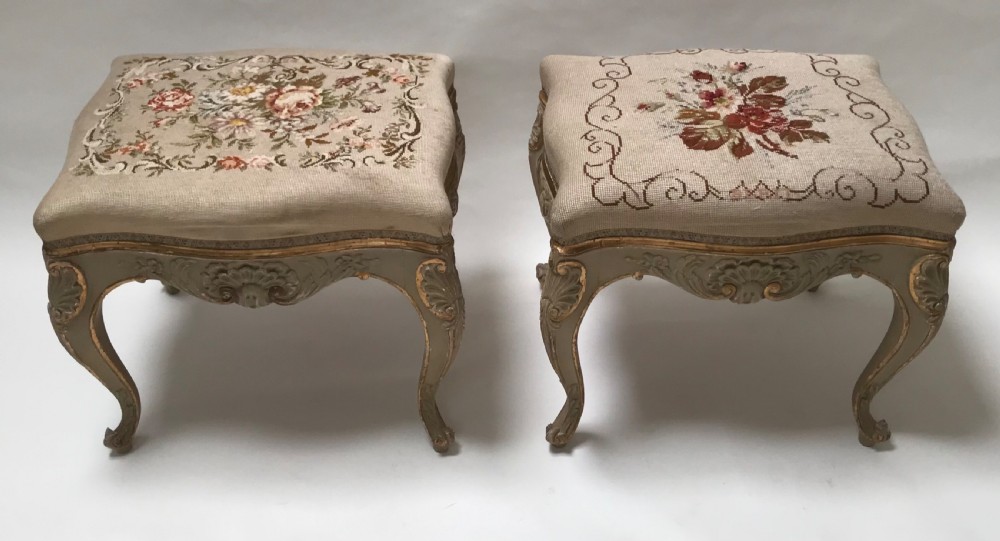 A pair of French Louis XV style footstools with painted cabriole legs, gilded accents, and floral needlepoint upholstery.