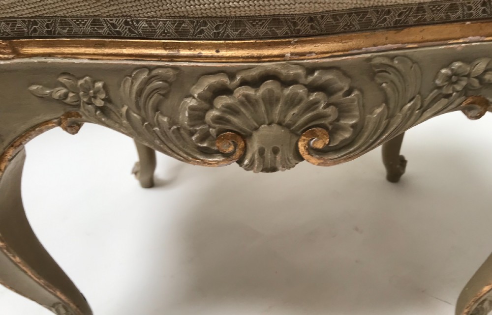 A pair of French Louis XV style footstools with painted cabriole legs, gilded accents, and floral needlepoint upholstery. View II