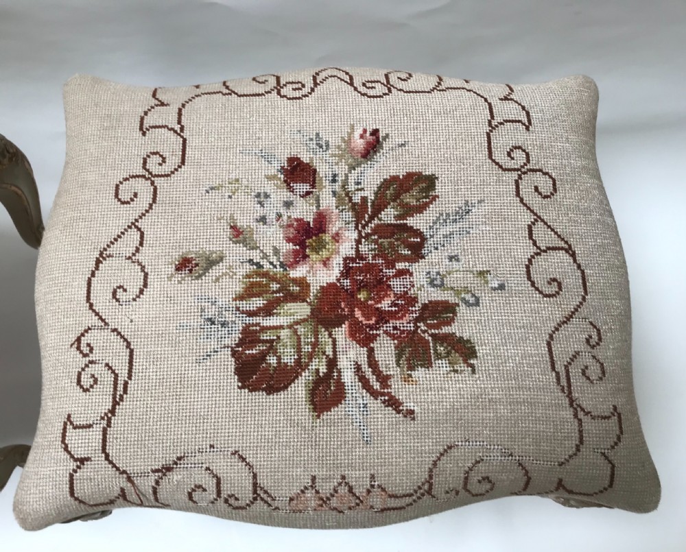 A pair of French Louis XV style footstools with painted cabriole legs, gilded accents, and floral needlepoint upholstery. View V