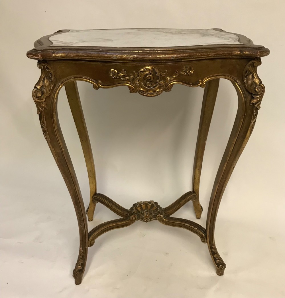 A French Louis XV style giltwood side table featuring a contoured white marble top, carved cabriole legs, and an X-shaped stretcher with a central shell motif.
