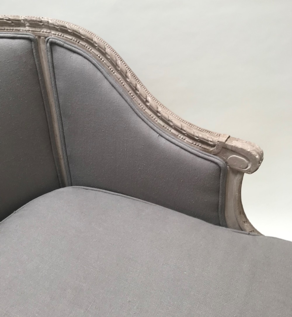 A French Louis XVI style upholstered daybed featuring a carved taupe-grey timber frame, fluted legs, a grey cushion seat, and a floral accent pillow. View IV
