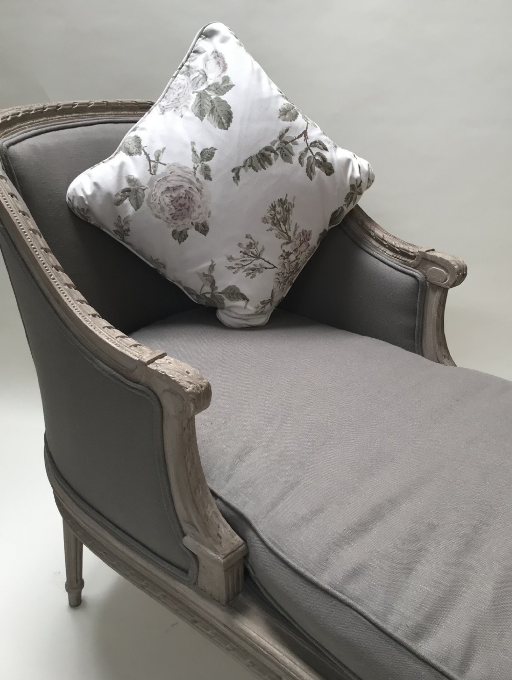 A French Louis XVI style upholstered daybed featuring a carved taupe-grey timber frame, fluted legs, a grey cushion seat, and a floral accent pillow. View V