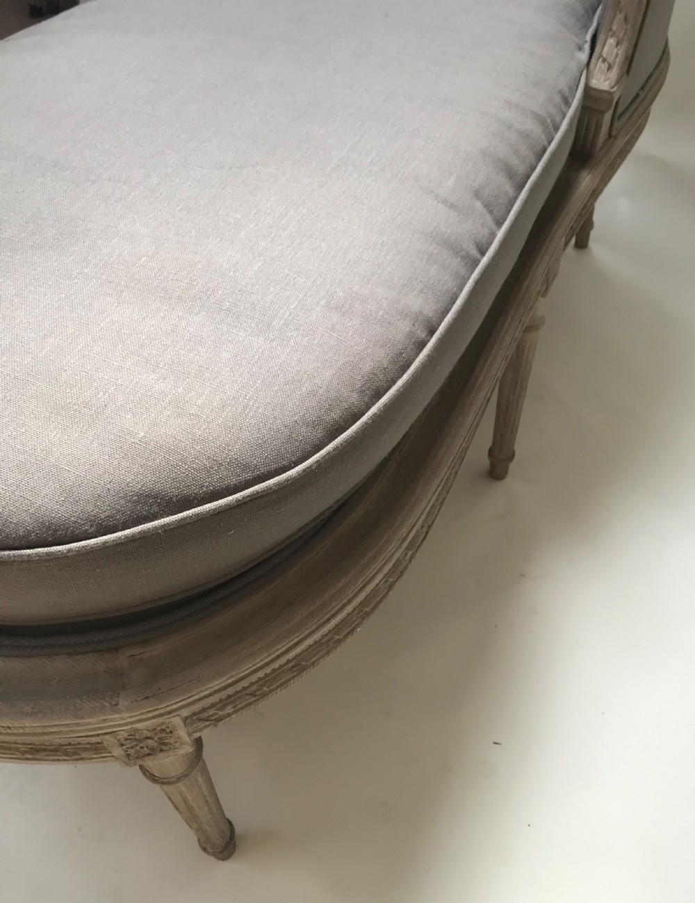 A French Louis XVI style upholstered daybed featuring a carved taupe-grey timber frame, fluted legs, a grey cushion seat, and a floral accent pillow. View VI