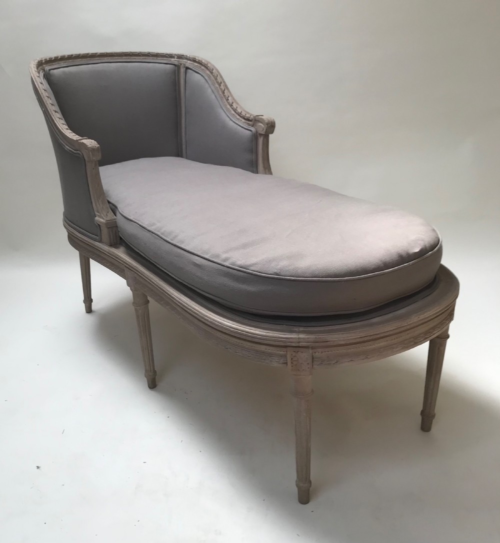 A French Louis XVI style upholstered daybed featuring a carved taupe-grey timber frame, fluted legs, a grey cushion seat, and a floral accent pillow. View XI