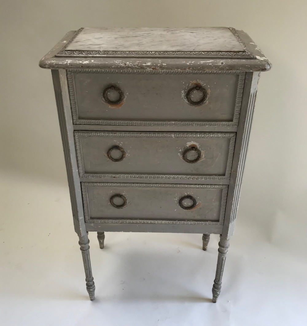 A tall, narrow French grey painted chest of three drawers featuring ring pulls, detailed trim moulding, turned legs, and an inset marble top. View II