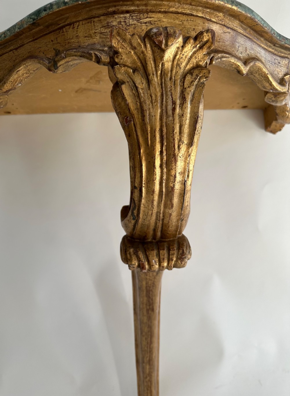 A wall-mounted Italian gilded console table featuring a single curved carved leg and a dark green marble top. View III