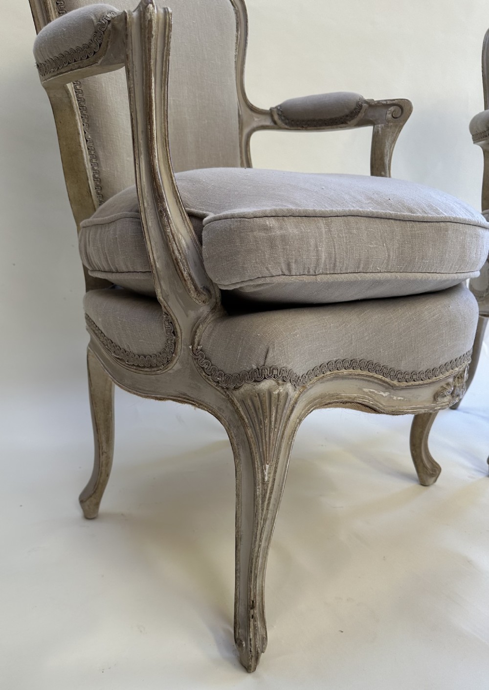 A pair of French Louis XV style open armchairs with grey painted carved wooden frames and neutral linen upholstery. View IV