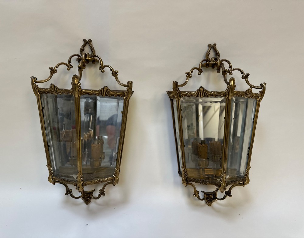 A pair of French antique gilt brass and bevelled glass wall lanterns featuring ornamental scrollwork crests and internal candle-style light fittings. View III