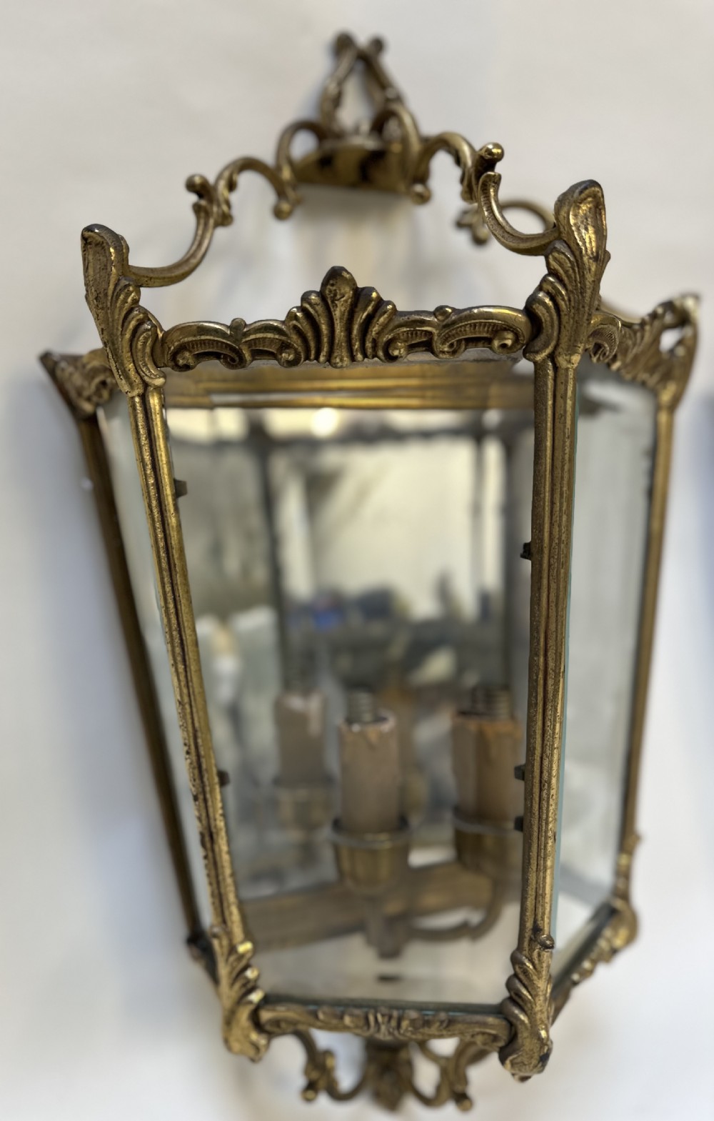 A pair of French antique gilt brass and bevelled glass wall lanterns featuring ornamental scrollwork crests and internal candle-style light fittings. View VI