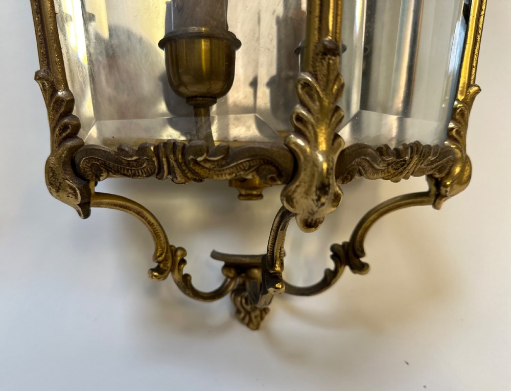 A pair of French antique gilt brass and bevelled glass wall lanterns featuring ornamental scrollwork crests and internal candle-style light fittings. View VII