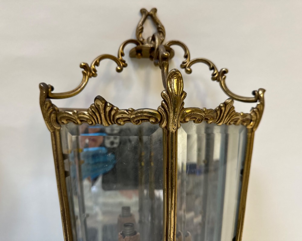 A pair of French antique gilt brass and bevelled glass wall lanterns featuring ornamental scrollwork crests and internal candle-style light fittings. View VIII