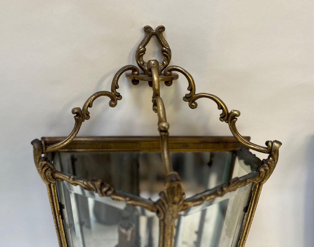 A pair of French antique gilt brass and bevelled glass wall lanterns featuring ornamental scrollwork crests and internal candle-style light fittings. View IX