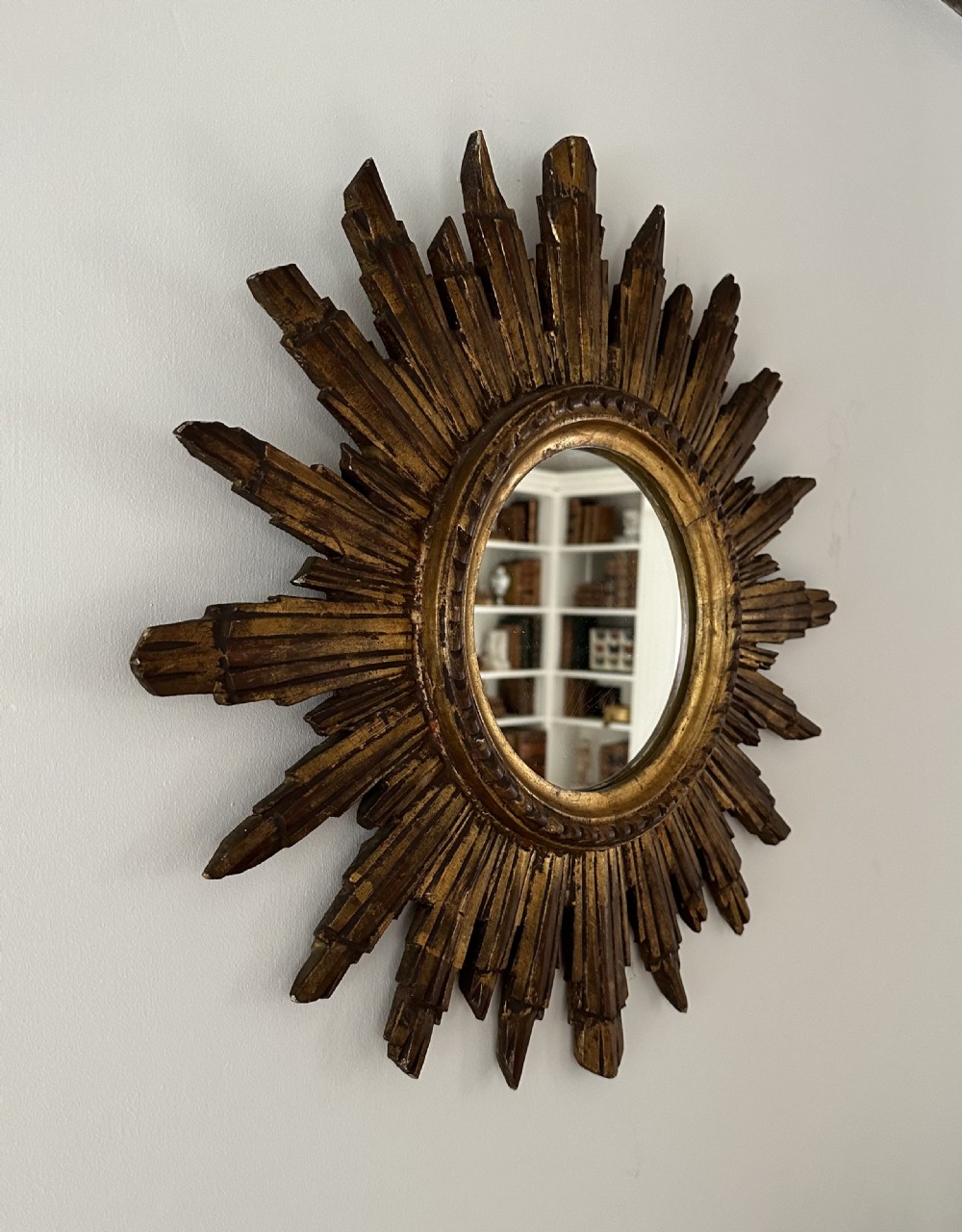 A circular wall mirror set within a gilded wooden frame featuring radiating, multi-tiered sunburst rays. View II