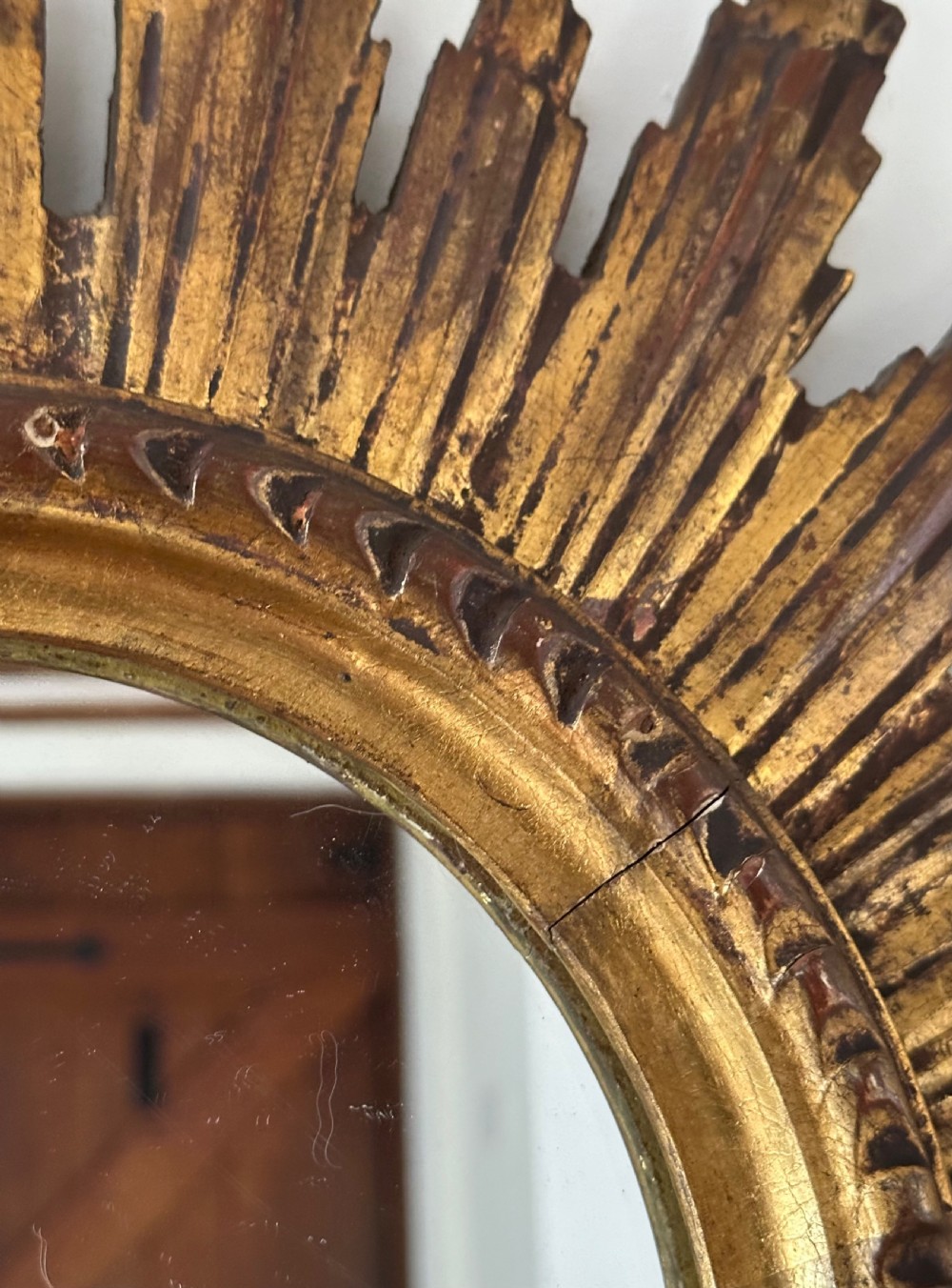 A circular wall mirror set within a gilded wooden frame featuring radiating, multi-tiered sunburst rays. View VII