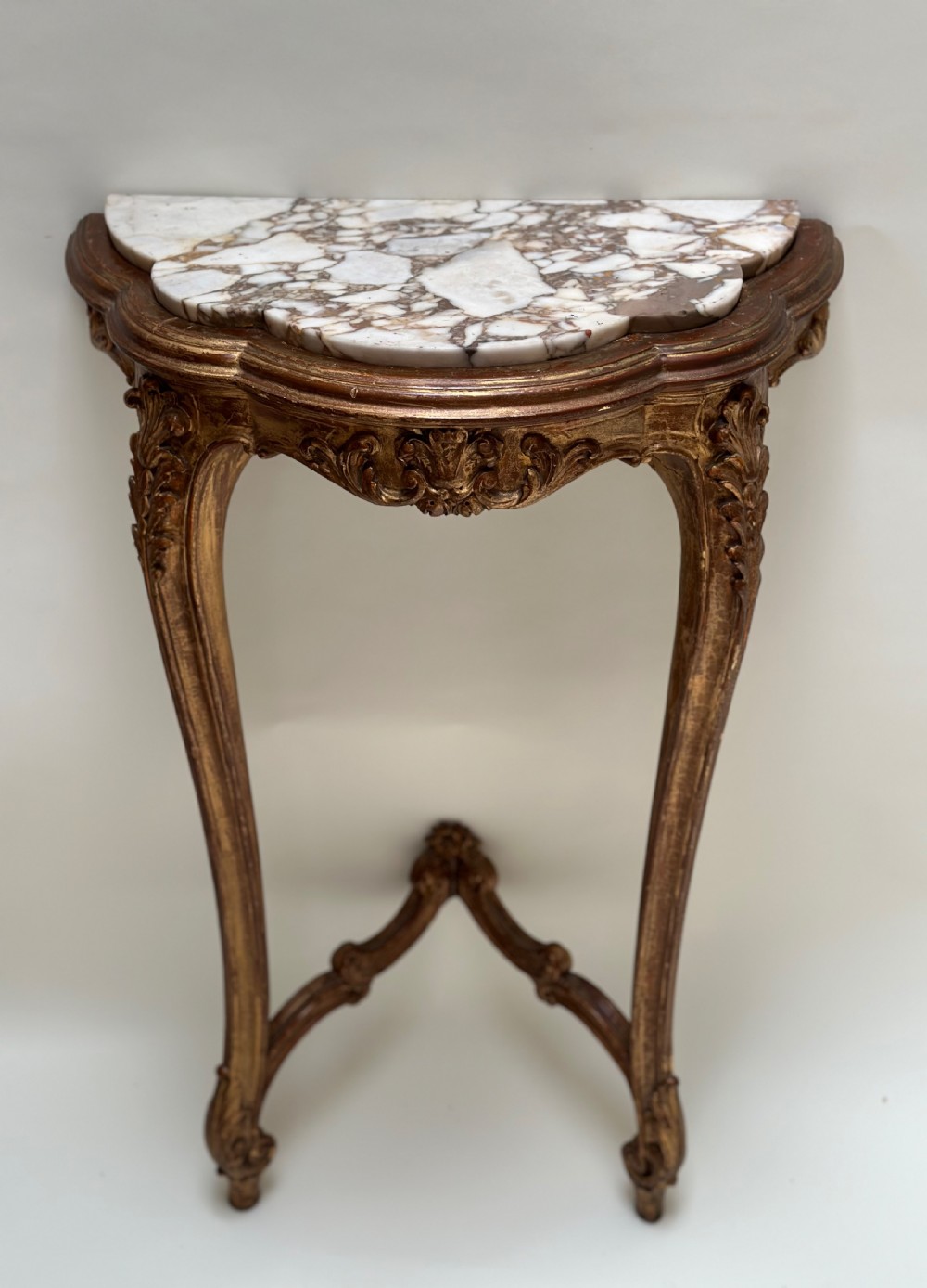 A French Rococo style demilune console table featuring a carved giltwood frame, cabriole legs with a stretcher base, and a veined marble top.