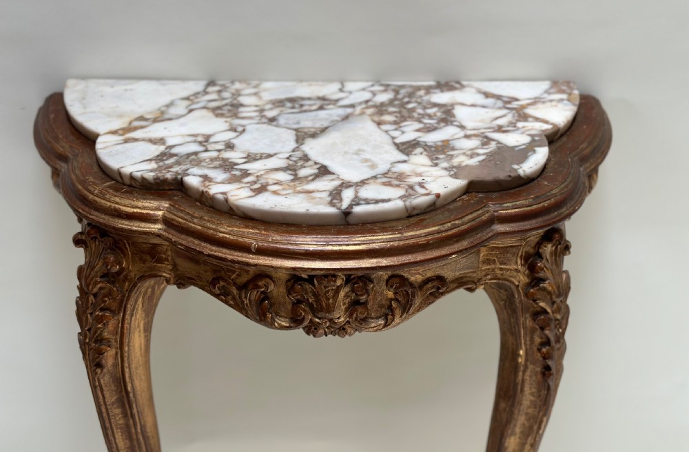 A French Rococo style demilune console table featuring a carved giltwood frame, cabriole legs with a stretcher base, and a veined marble top. View II