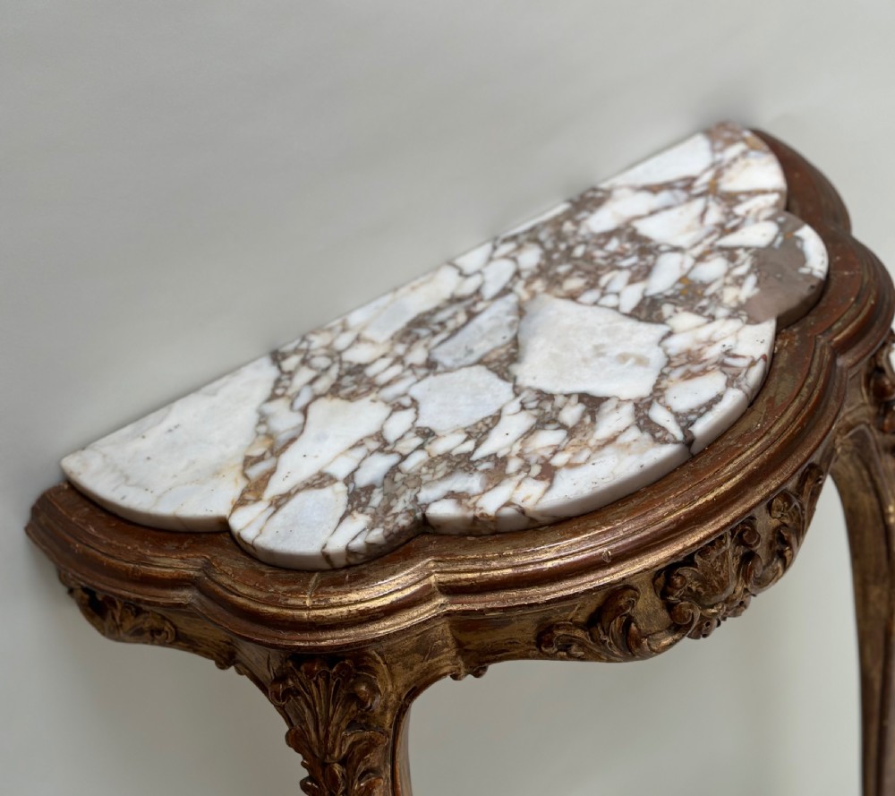 A French Rococo style demilune console table featuring a carved giltwood frame, cabriole legs with a stretcher base, and a veined marble top. View V