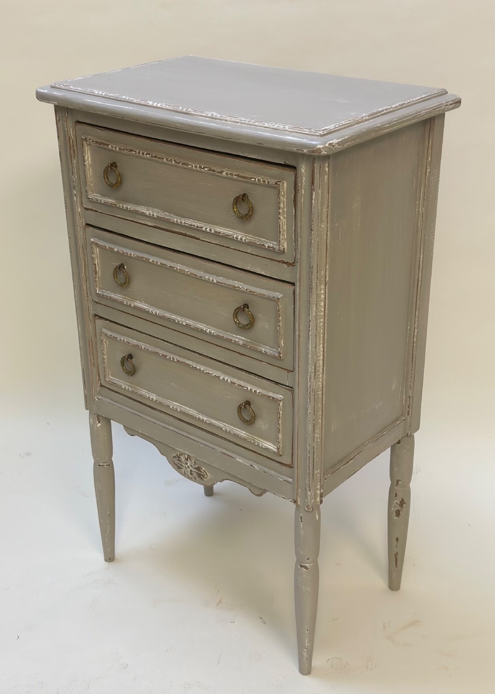 A small grey painted French-style chest with three drawers, brass ring handles, distressed edges, and tall turned legs. View V