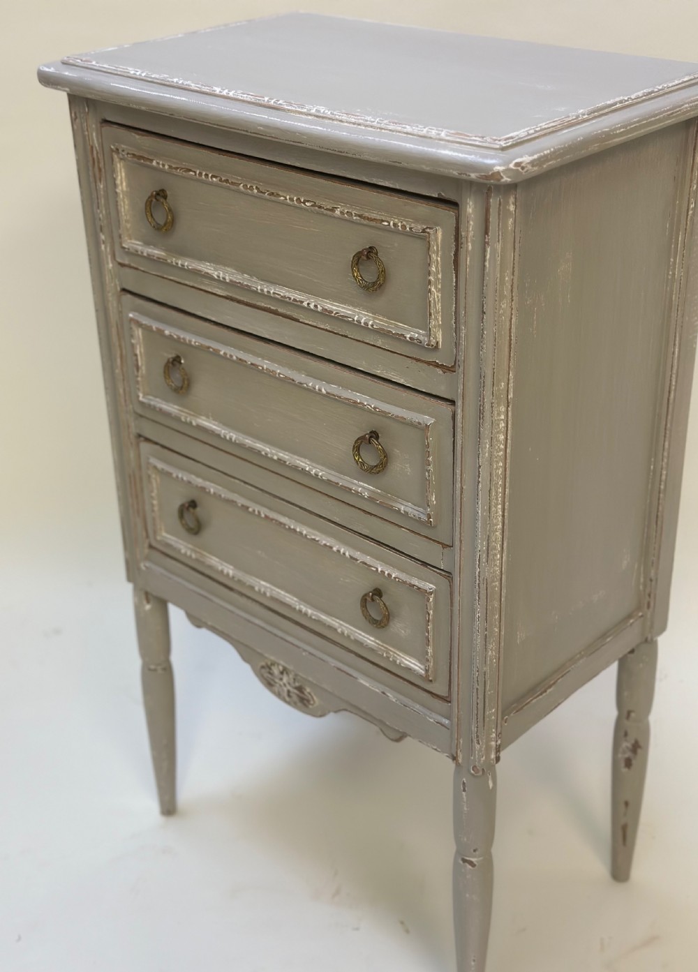 A small grey painted French-style chest with three drawers, brass ring handles, distressed edges, and tall turned legs. View VI