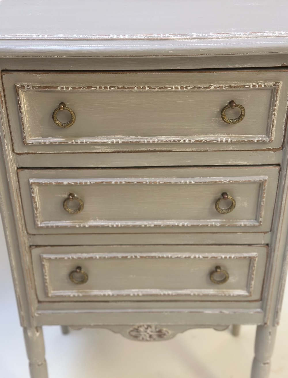 A small grey painted French-style chest with three drawers, brass ring handles, distressed edges, and tall turned legs. View VII