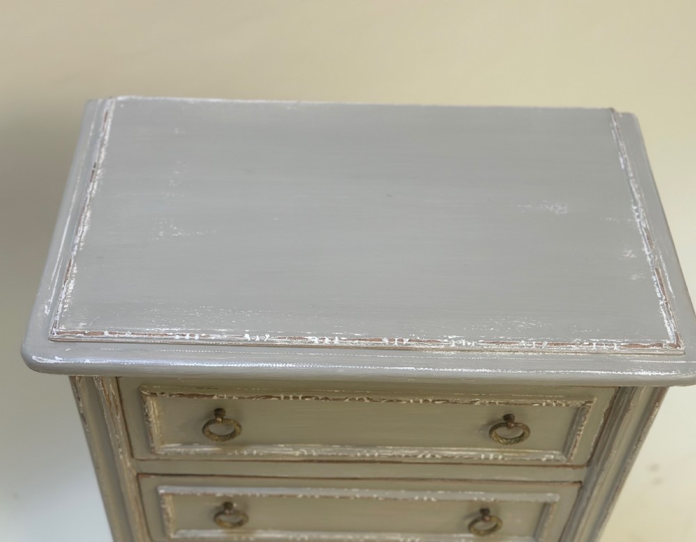 A small grey painted French-style chest with three drawers, brass ring handles, distressed edges, and tall turned legs. View VIII