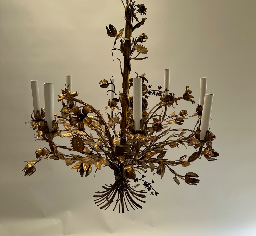 A multi-arm gilt metal chandelier featuring hand-worked botanical leaves, stems, flowers, and white tubular candle sleeves.