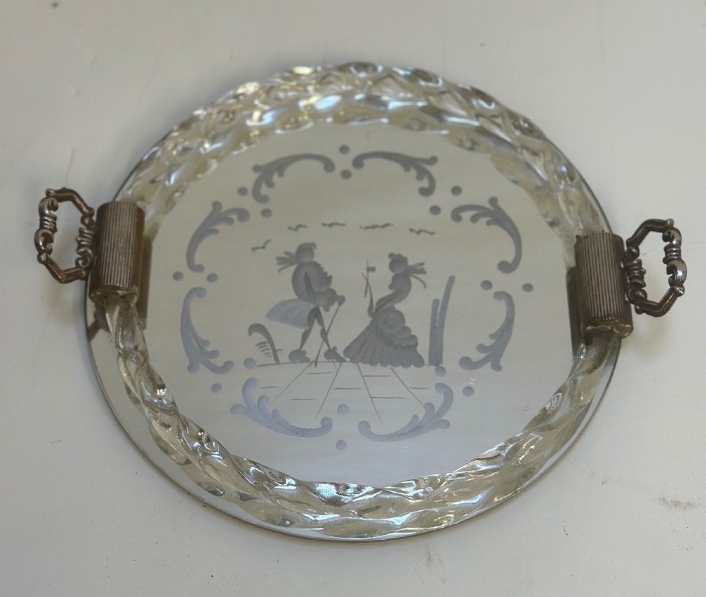 A circular Murano glass tray featuring a mirrored surface with an etched Venetian figure scene, framed by a twisted clear glass rim and two metal handles.