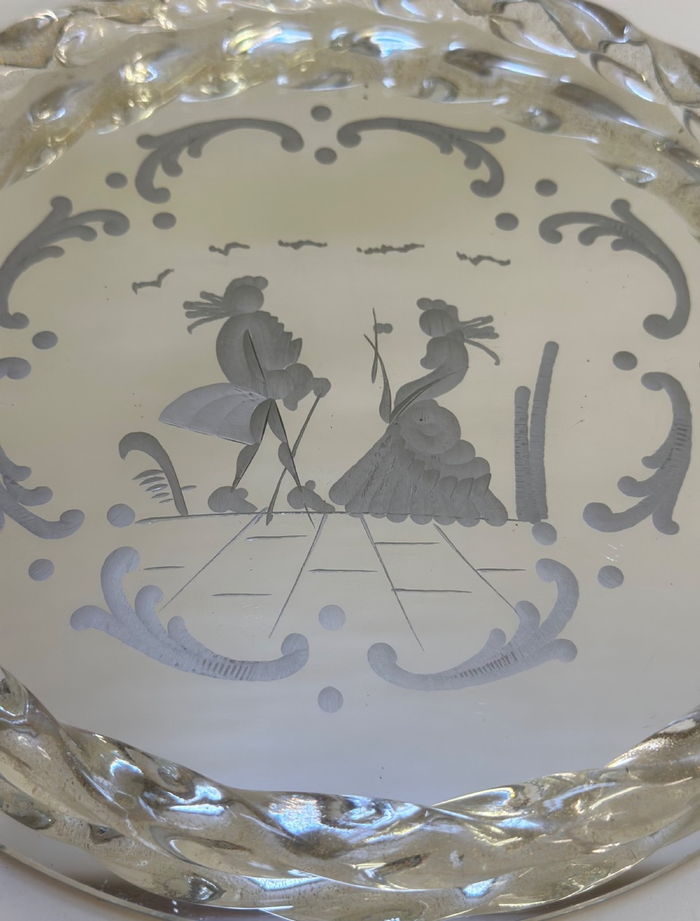 A circular Murano glass tray featuring a mirrored surface with an etched Venetian figure scene, framed by a twisted clear glass rim and two metal handles. View II