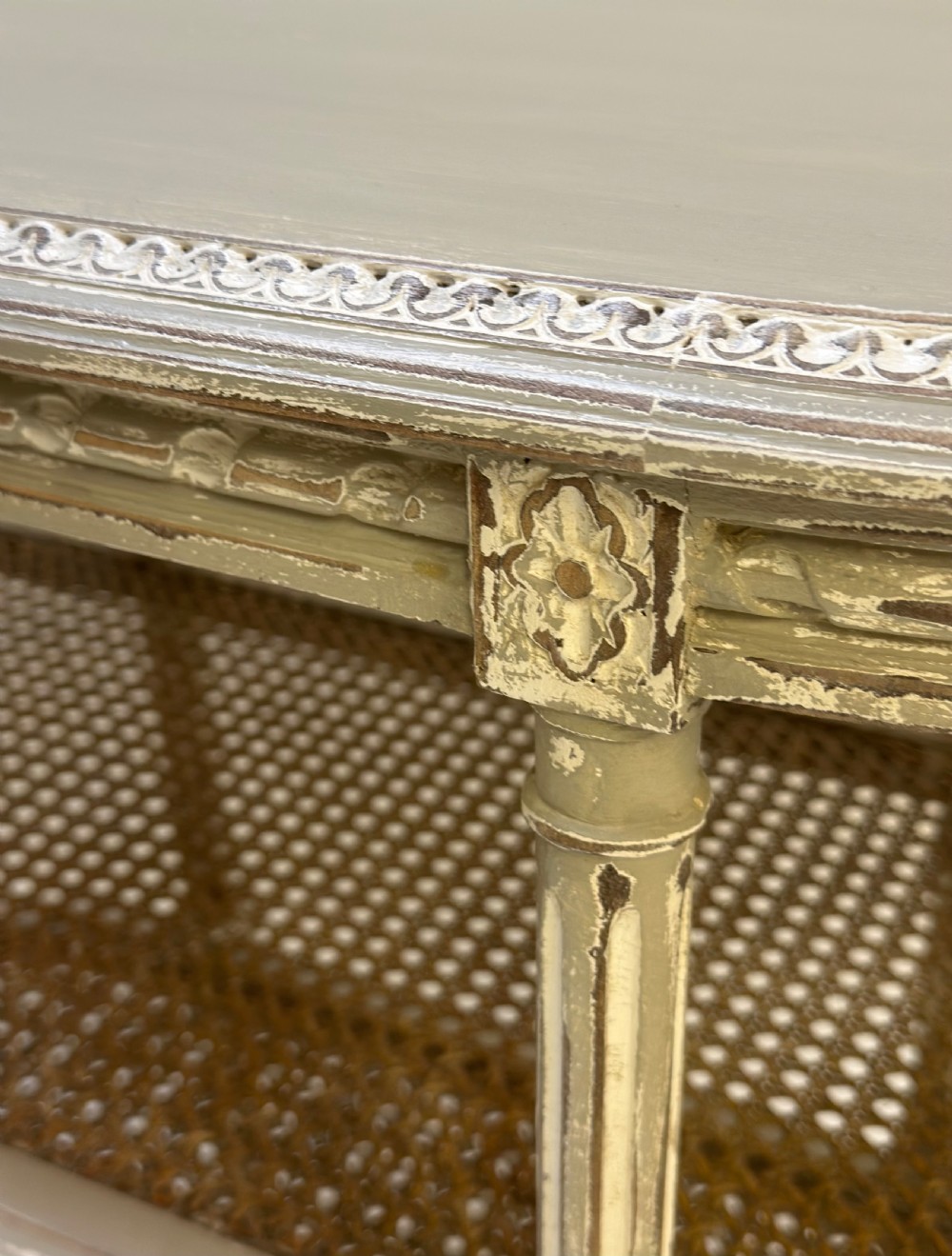 An oval French-style tiered side table painted in distressed grey with fluted legs, carved rosettes, and two cane lower shelves. View III