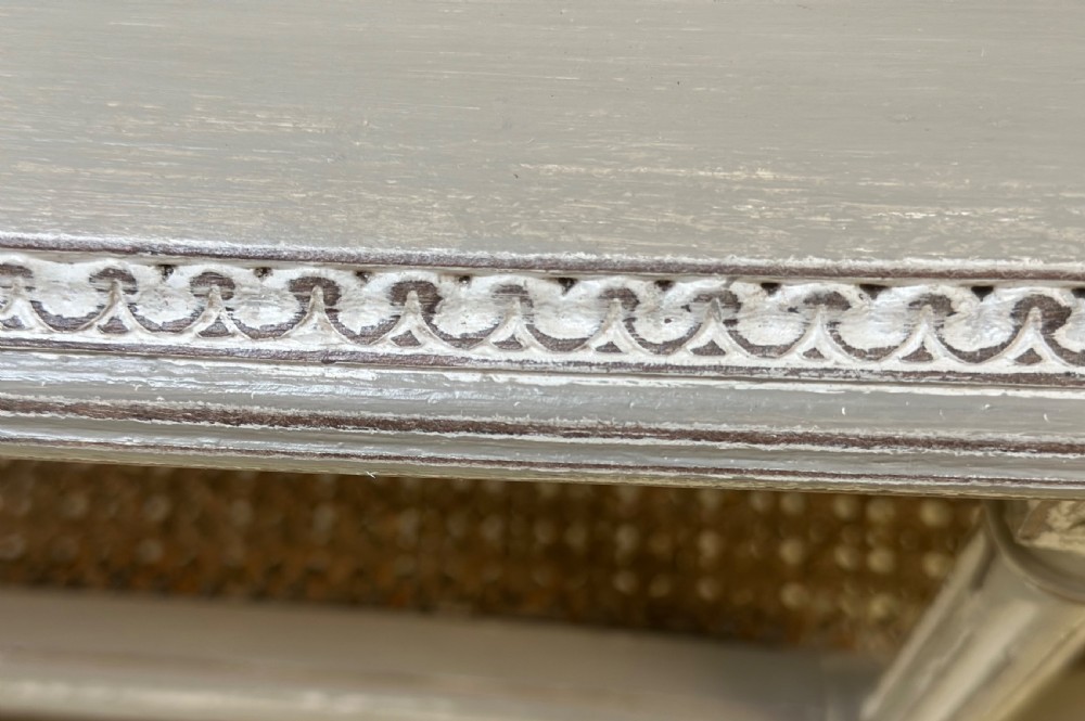 An oval French-style tiered side table painted in distressed grey with fluted legs, carved rosettes, and two cane lower shelves. View VI