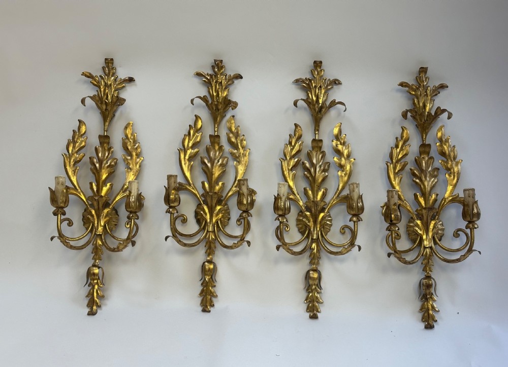 A set of four French gilded metal two-light wall sconces featuring scrolled acanthus leaf backplates and candle-style sconce arms.