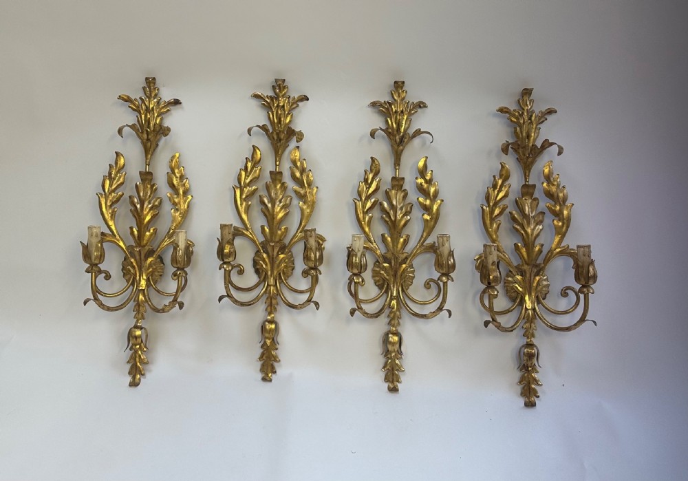 A set of four French gilded metal two-light wall sconces featuring scrolled acanthus leaf backplates and candle-style sconce arms. View X