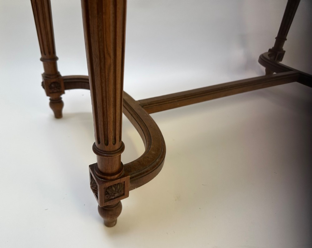 A rectangular French Neoclassical style stool featuring light grey linen upholstery, carved frieze woodwork, fluted legs, and a curved stretcher. View II