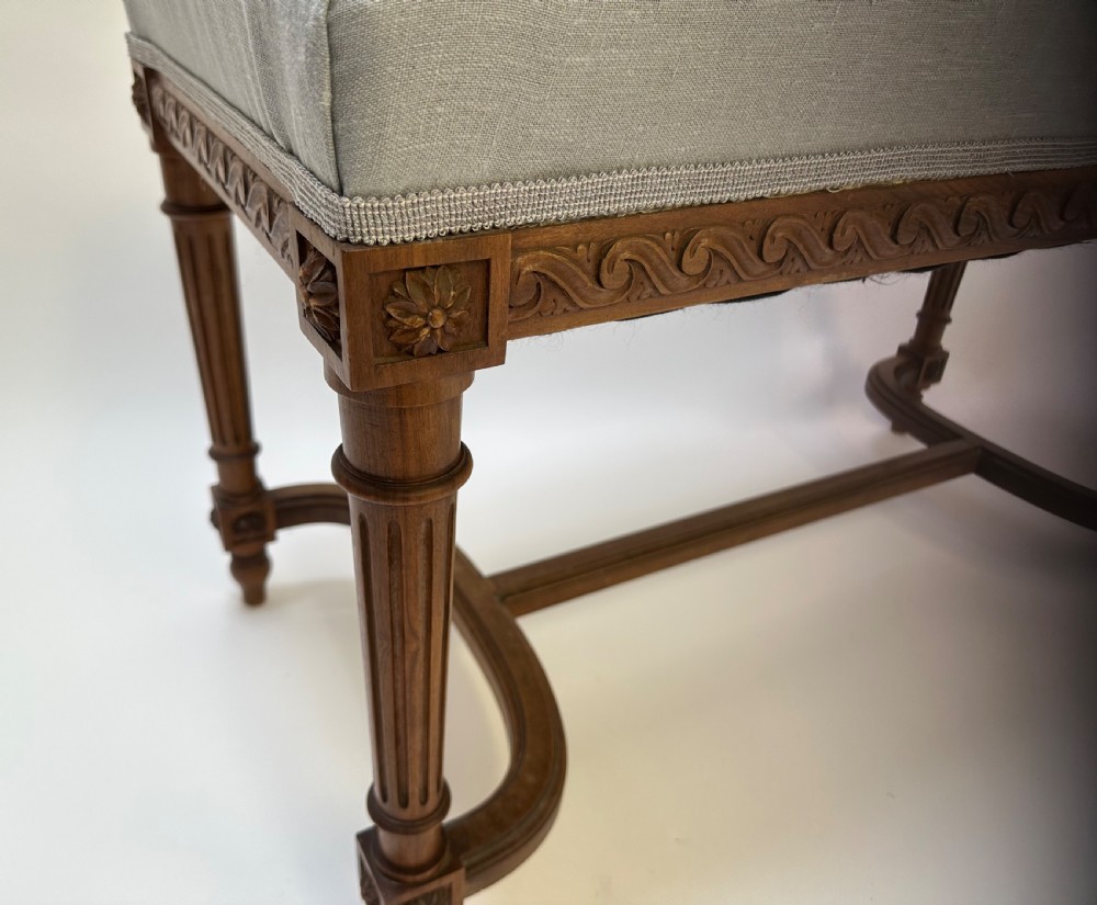 A rectangular French Neoclassical style stool featuring light grey linen upholstery, carved frieze woodwork, fluted legs, and a curved stretcher. View III