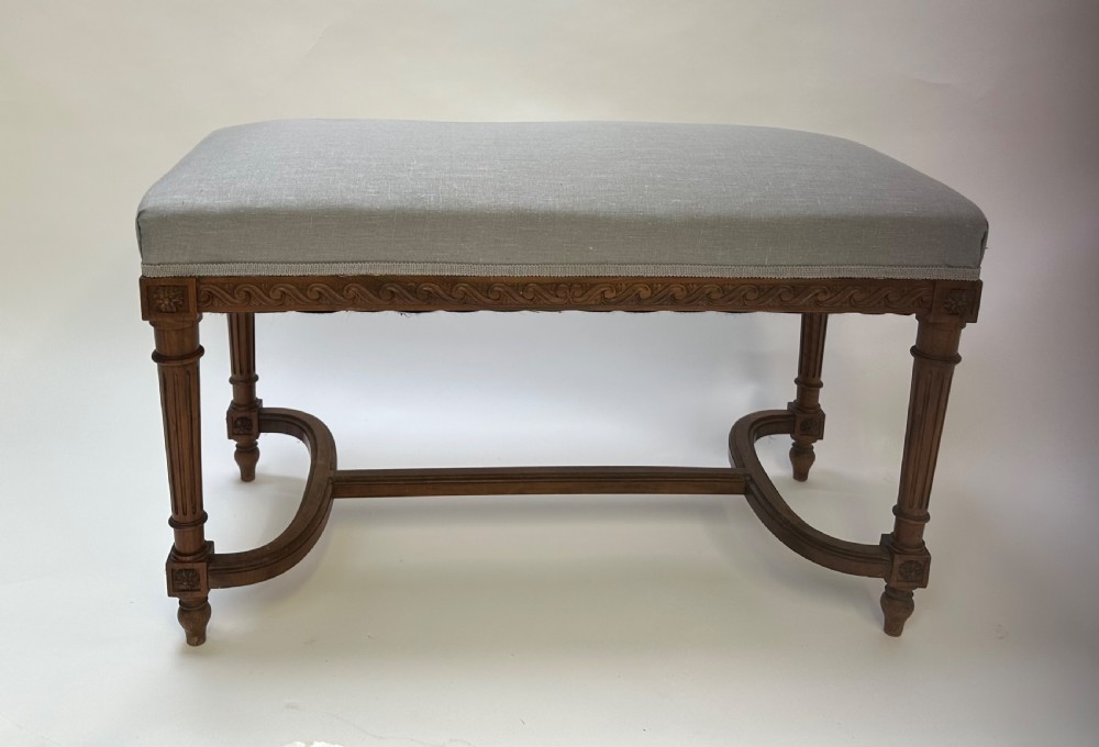 A rectangular French Neoclassical style stool featuring light grey linen upholstery, carved frieze woodwork, fluted legs, and a curved stretcher. View VII