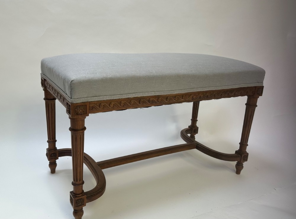 A rectangular French Neoclassical style stool featuring light grey linen upholstery, carved frieze woodwork, fluted legs, and a curved stretcher. View VIII