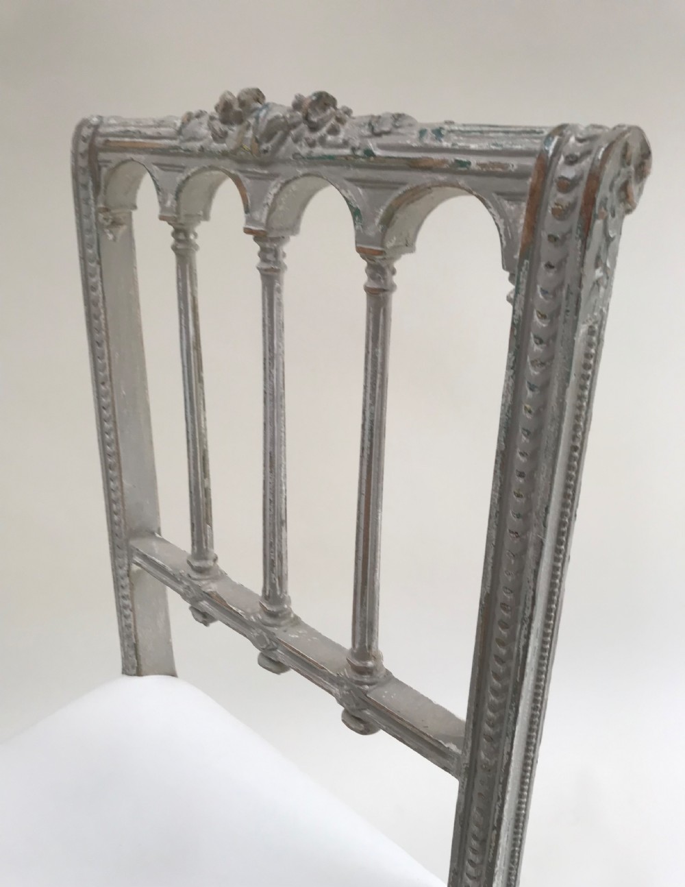 A pair of French Louis XVI style side chairs featuring distressed grey painted wooden frames, carved arcade backrests, and neutral white upholstered seats. View VIII