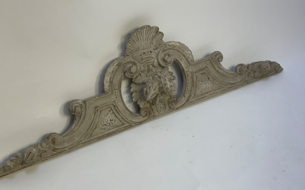 An antique French grey painted wooden pelmet featuring central hand-carved foliage and detailed scrollwork.