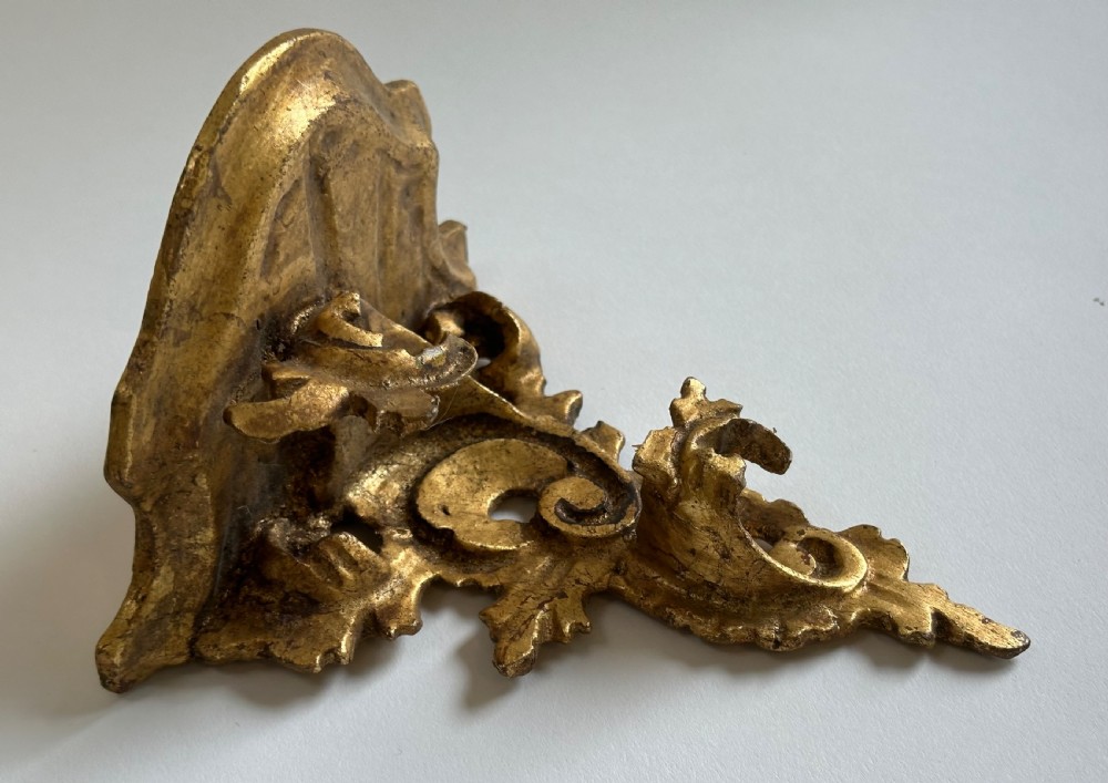 A pair of carved wood wall brackets with a hand-gilded gold finish featuring acanthus leaf scrollwork and flat top shelves. View IV